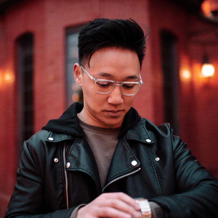 Man wearing glasses and a dark jacket in front of a red brick wall.