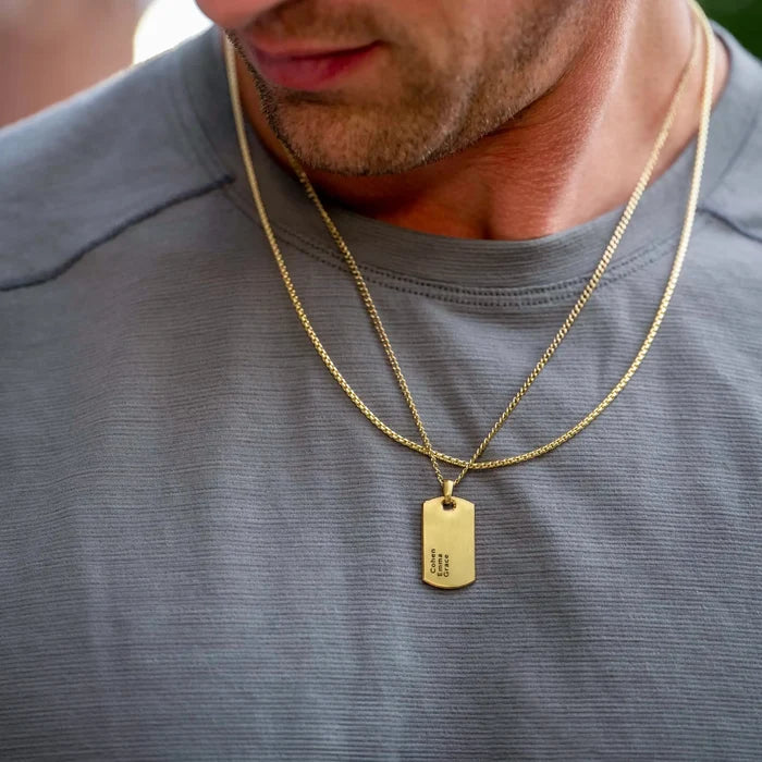 Man wearing a gold necklace with a dog tag on a gray shirt