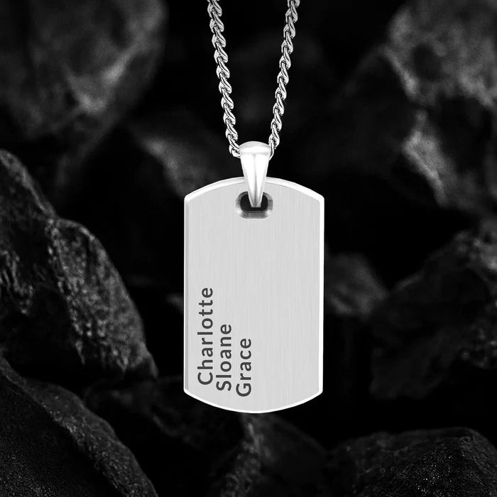 Silver dog tag necklace with engraved names on a dark textured background