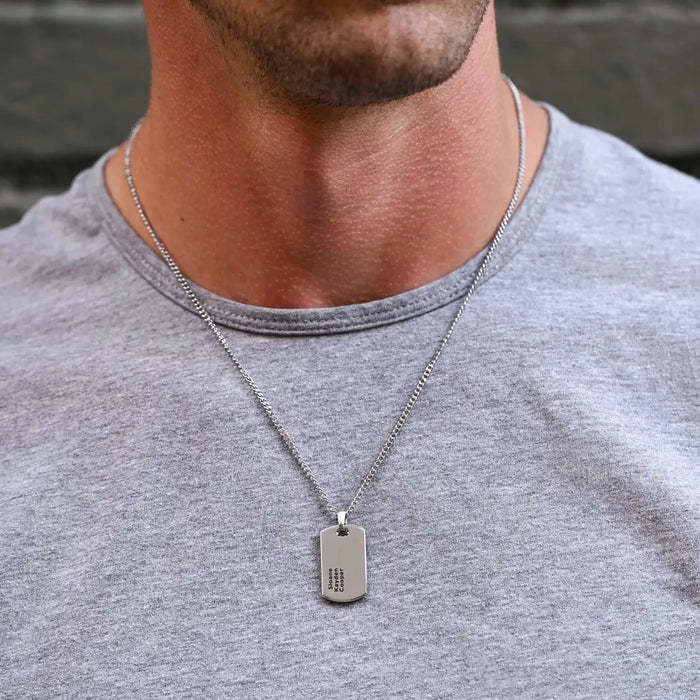 Man wearing a gray shirt with a silver necklace featuring a dog tag.