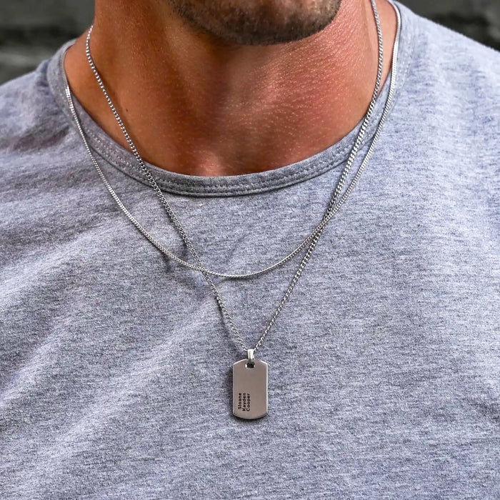 Close-up of a person wearing a silver necklace with a dog tag on a gray shirt.