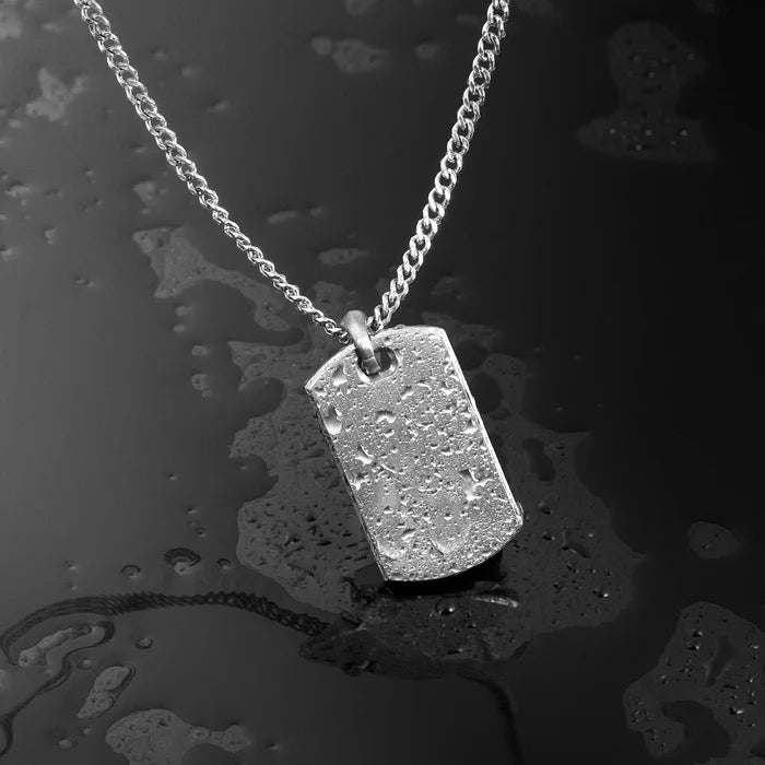 Silver dog tag necklace on a textured black surface