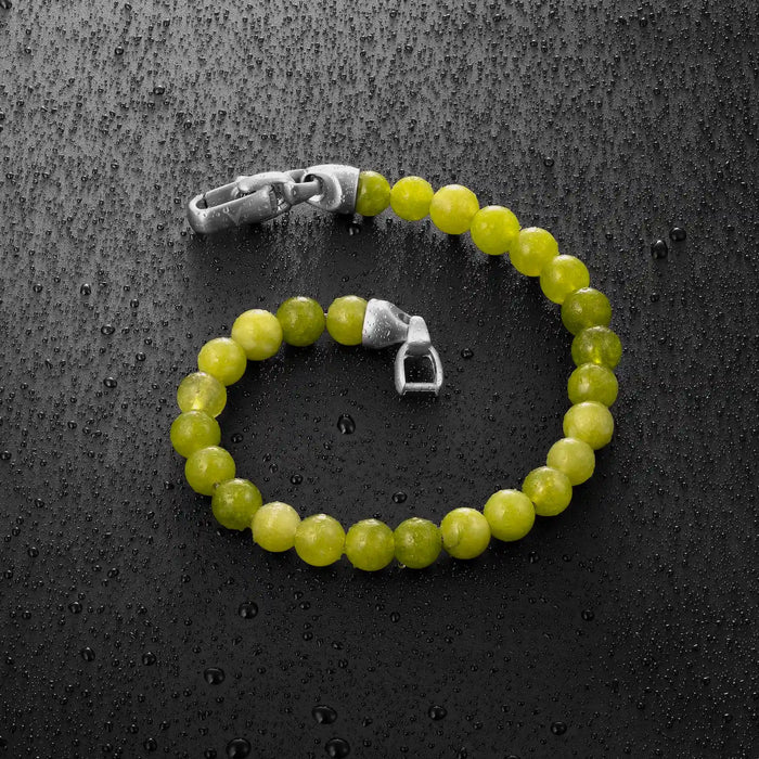 Green beaded bracelet with silver clasp on a textured black surface