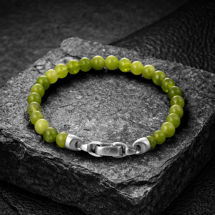 Green beaded bracelet with a silver clasp on a dark stone surface