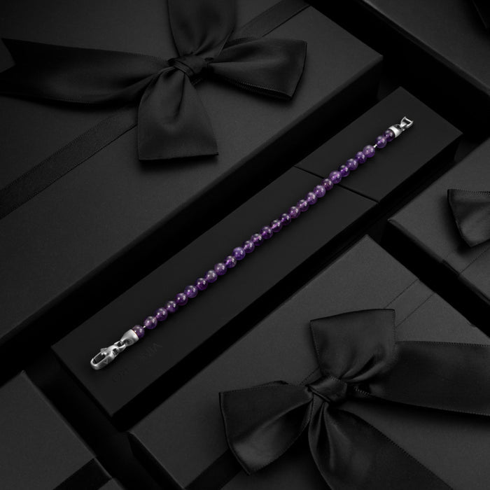 Purple beaded bracelet on a black surface with decorative bows