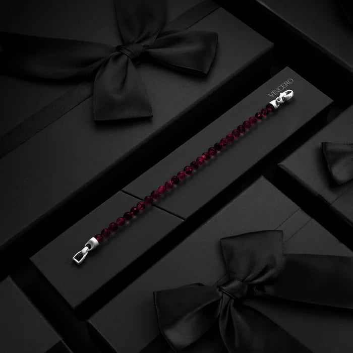 Red beaded bracelet with silver clasp on a black surface with decorative bows