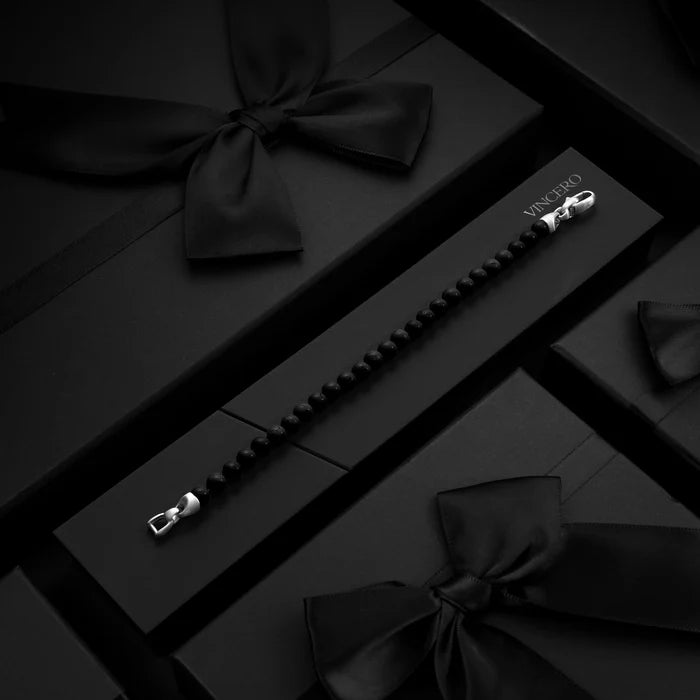 Black bow ties and a black bracelet with silver clasp on a dark surface