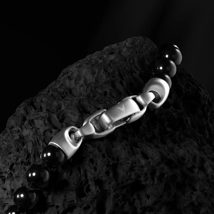 Black beaded bracelet with silver clasp on a textured black surface