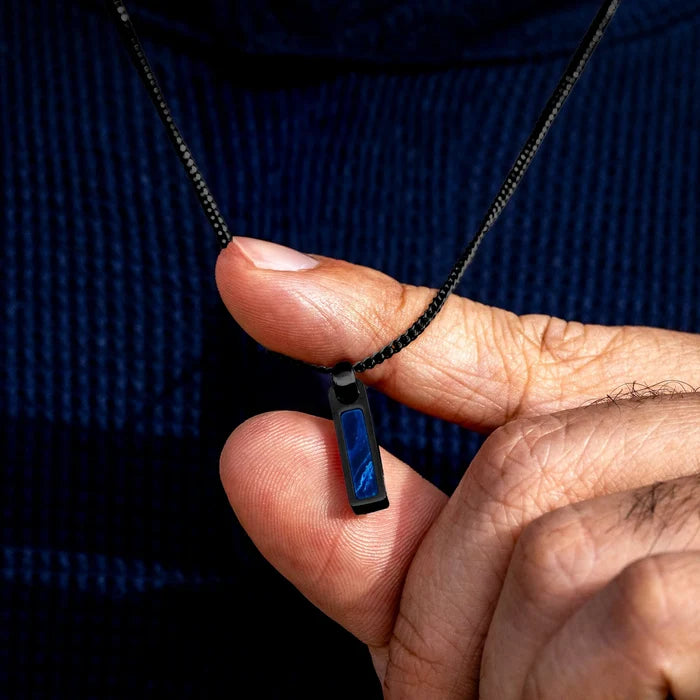 Hand holding a necklace with a blue pendant against a dark background