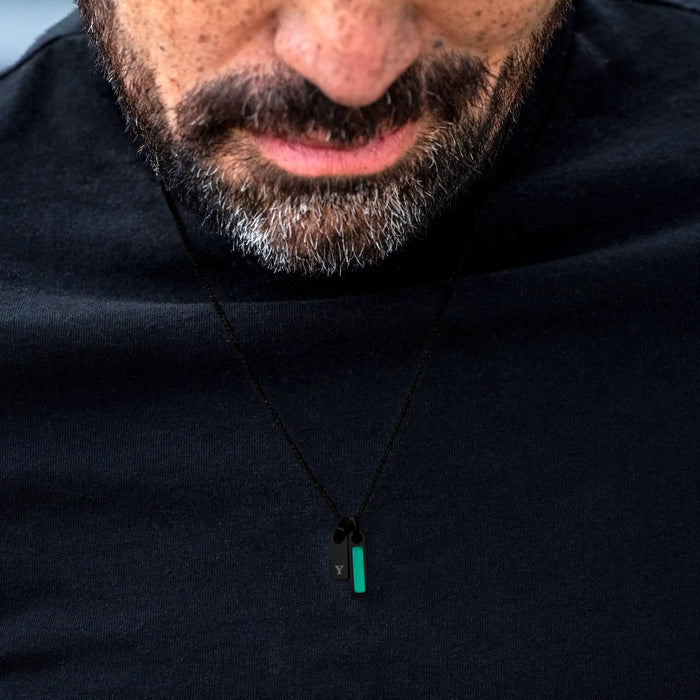 Close-up of a person wearing a black hoodie with a necklace featuring a green pendant.