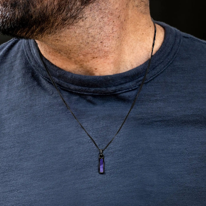 Person wearing a dark blue shirt with a necklace featuring a purple pendant.