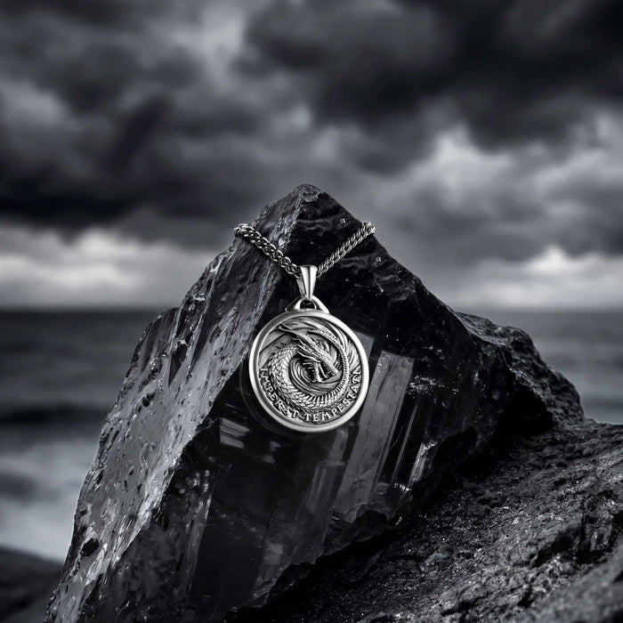 Silver pendant with dragon design on a rock against a stormy sky