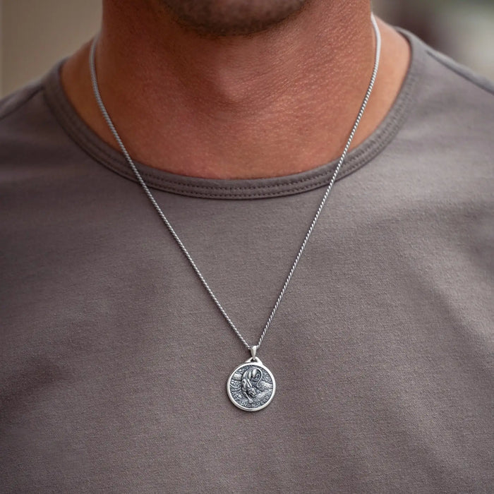 A silver coin pendant necklace worn by a man in a gray t-shirt. The pendant features an embossed design of a panther figure.