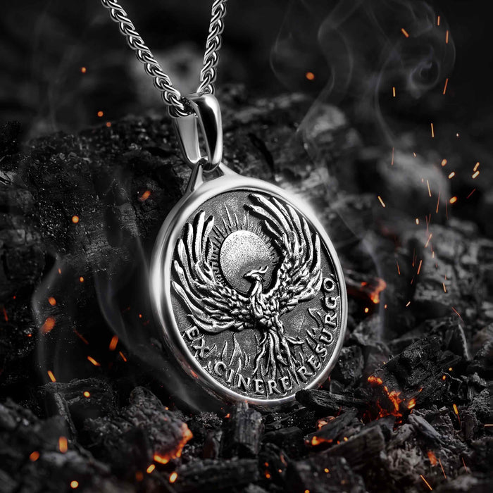 Silver pendant with a phoenix design on a dark background with flames.