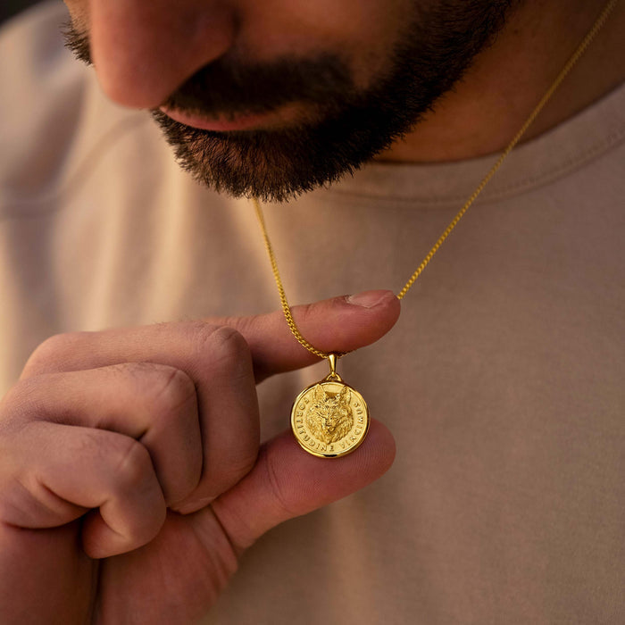 Man holding a gold necklace with a coin pendant against a neutral background