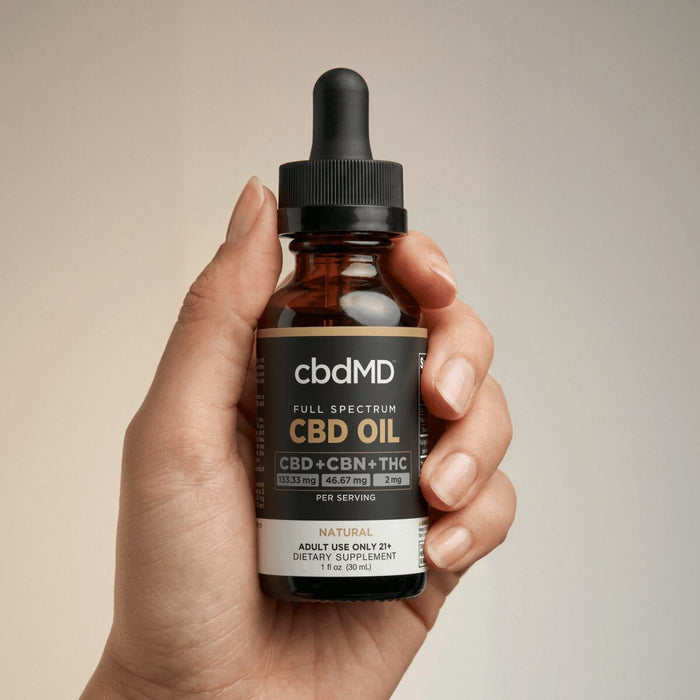 Hand holding full spectrum CBD oil tincture bottle with dropper, label showing CBD CBN THC blend.