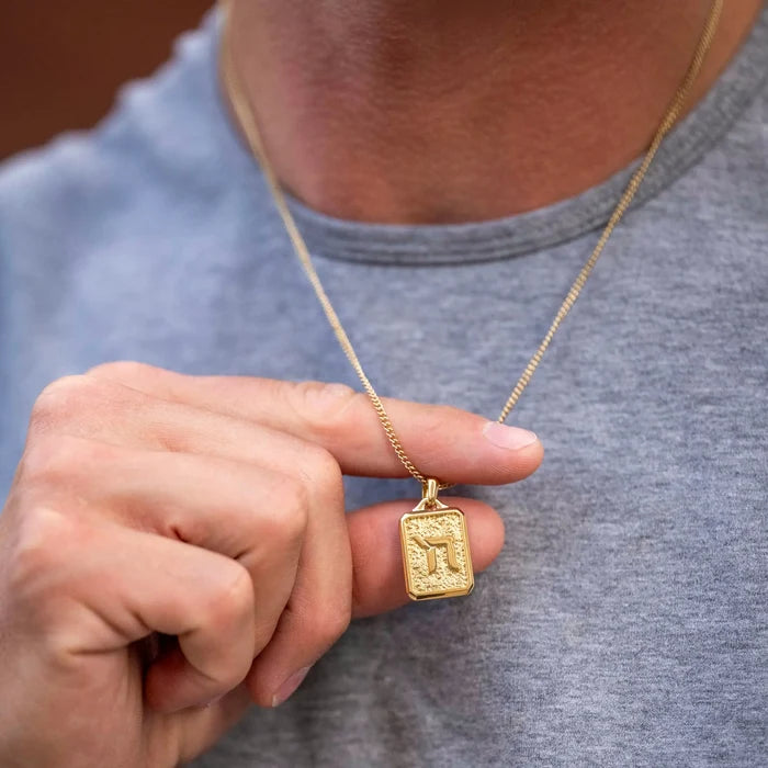 Gold necklace with a pendant held by a person wearing a gray shirt.