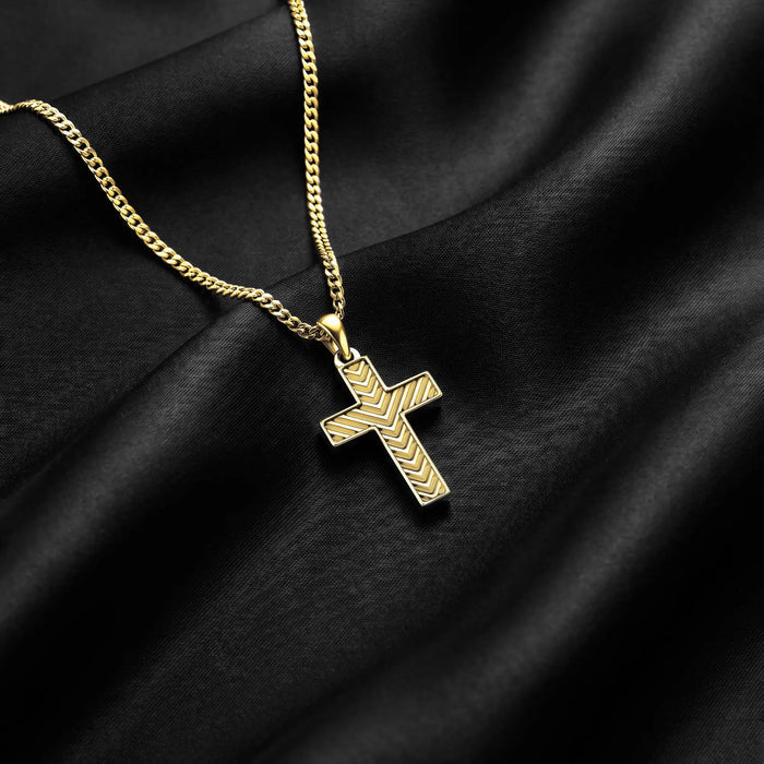 A gold cross pendant necklace with a textured chevron pattern, resting on draped black satin fabric.