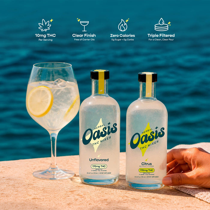 Two bottles of Oasis THC Minder unflavored and citrus tinctures are displayed on a sandy surface with a glass of cocktail in the background, set against a blue ocean backdrop. A hand is holding the right bottle.