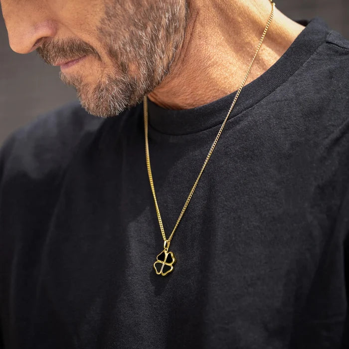 Man wearing a black shirt with a gold necklace featuring a clover pendant.