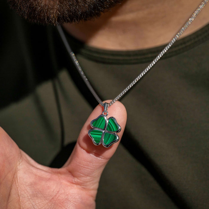 Green four-leaf clover pendant on a silver chain held by a hand.