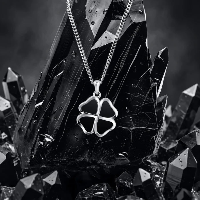 A silver-toned necklace with a four-leaf clover pendant, displayed on a large dark crystal cluster.