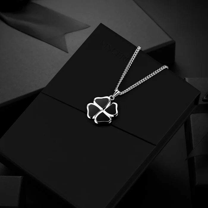 A silver-toned necklace with a four-leaf clover pendant, displayed on a black gift box against a dark background.