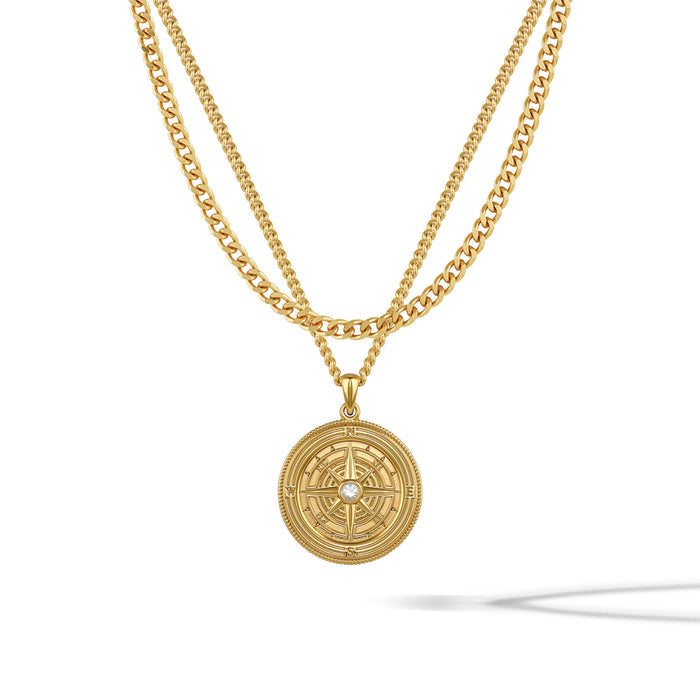 A gold-colored compass pendant necklace with a central sapphire stone, featuring a classic curb chain design.