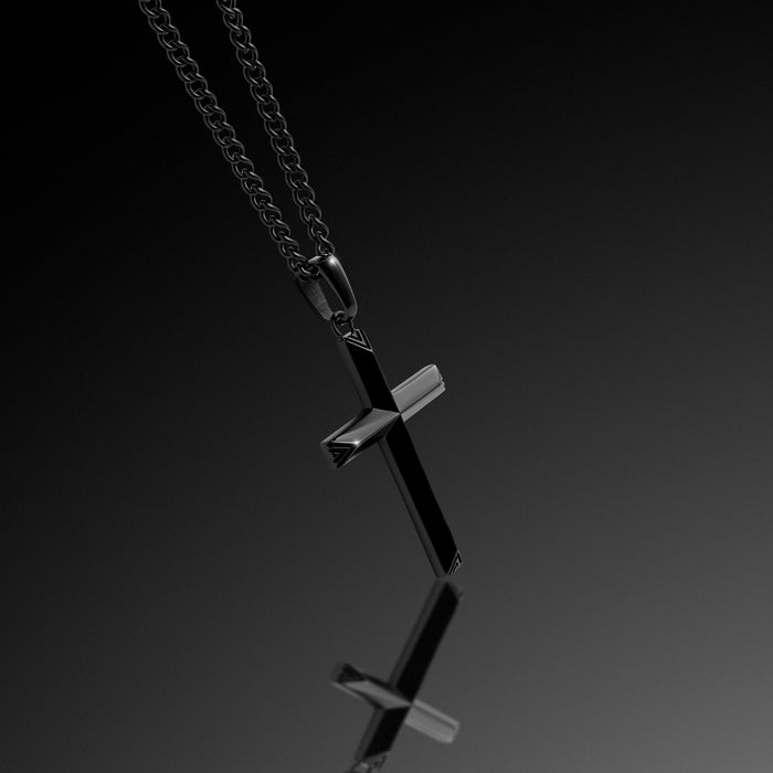 Black cross pendant on a chain against a dark background