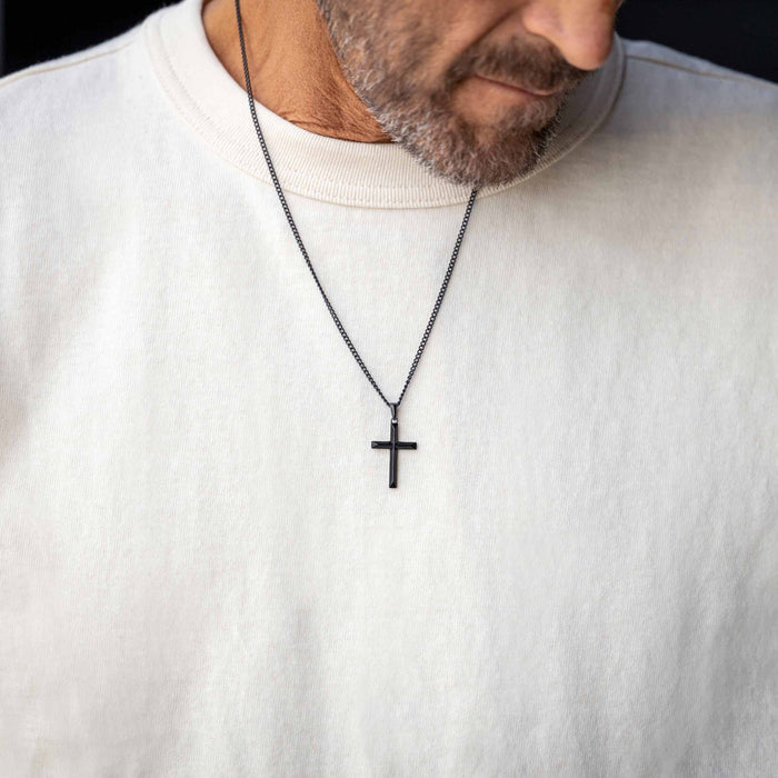 Man wearing a white sweater with a black cross necklace.
