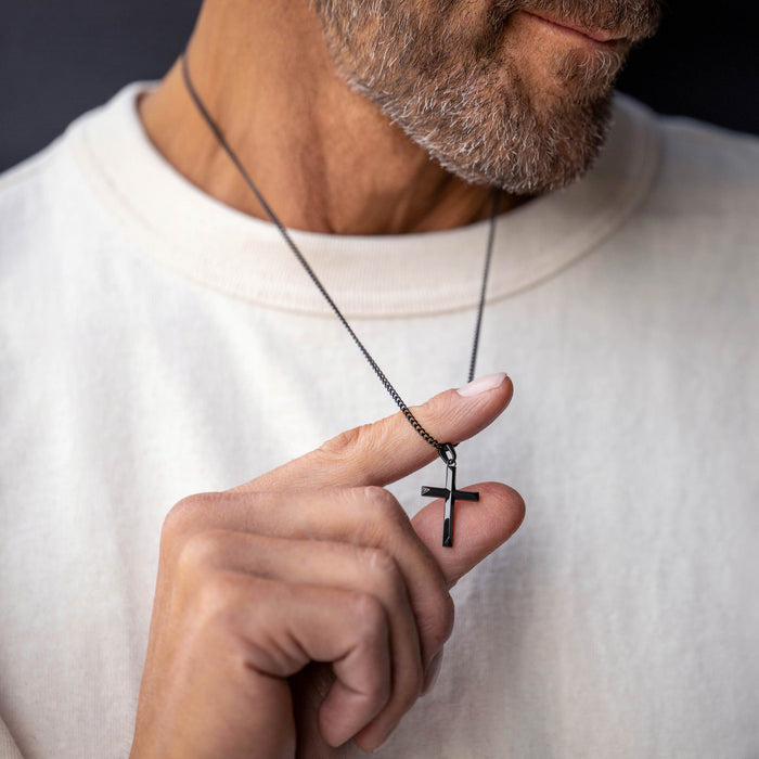 Man holding a necklace with a cross pendant against a neutral background