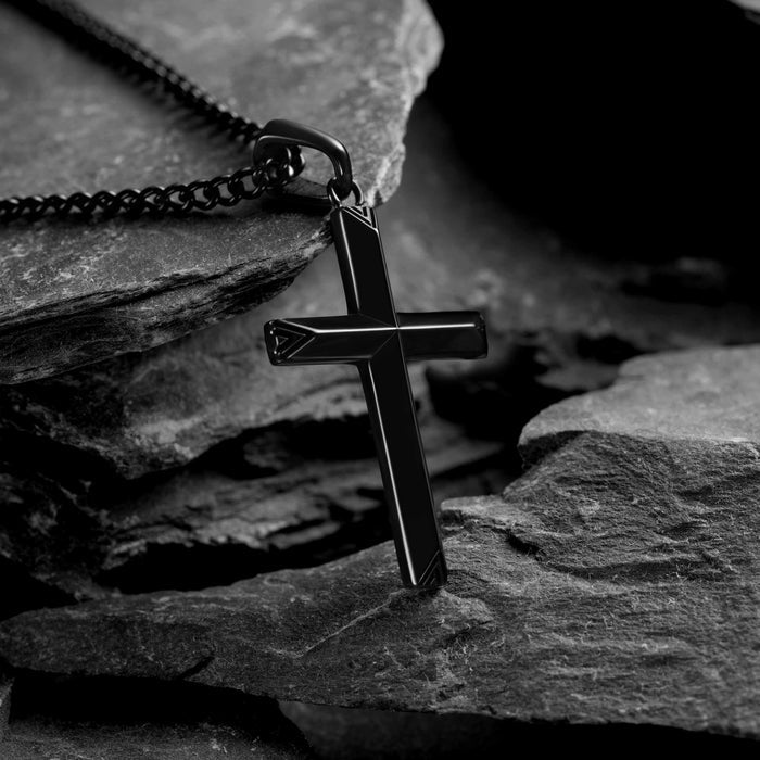 Black cross pendant on a chain resting on a stone surface