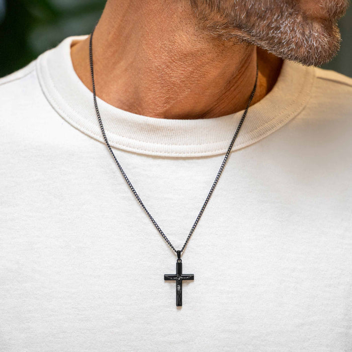 Man wearing a black cross necklace on a white shirt