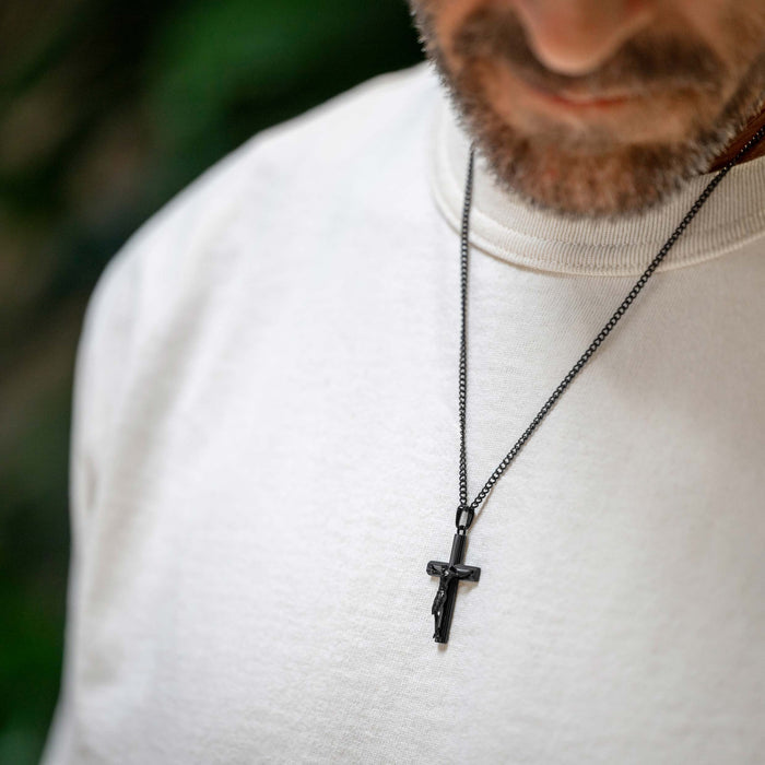 Man wearing a black cross necklace against a blurred background