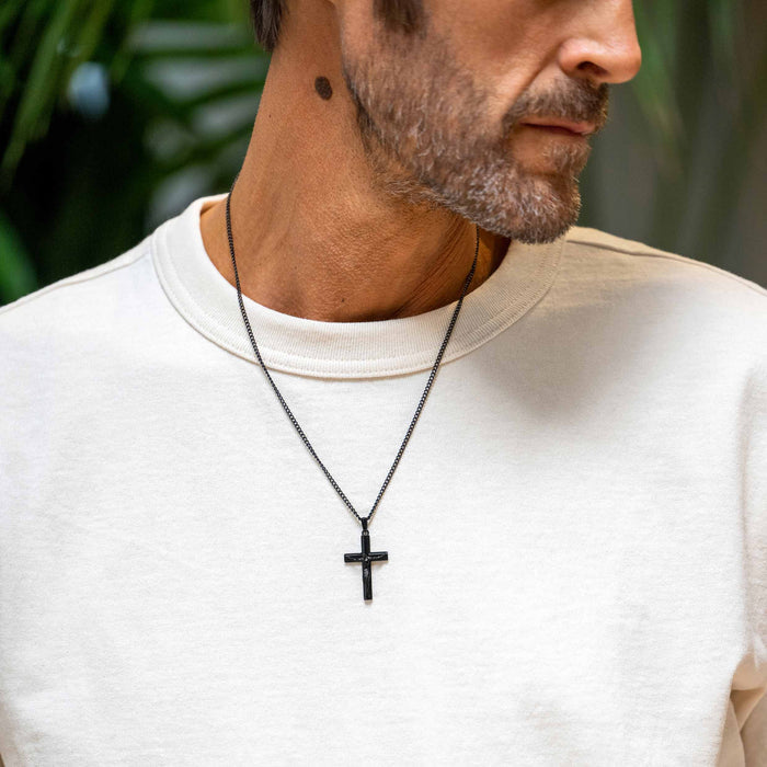Man wearing a black cross necklace against a blurred green background