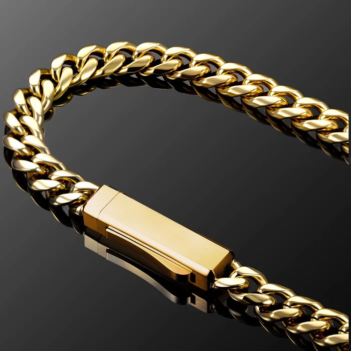A close-up of a gold Cuban link chain bracelet with a polished rectangular clasp, set against a dark reflective background.