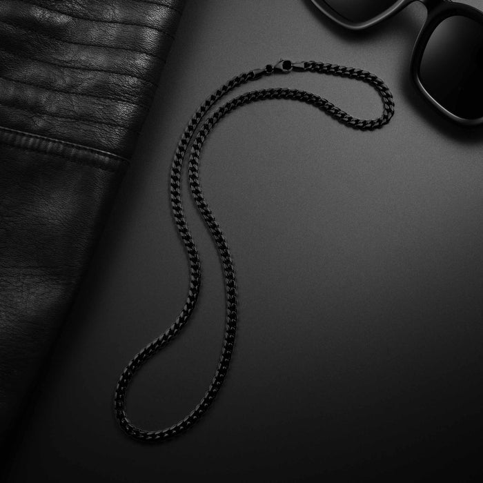 Black chain necklace on a dark surface with sunglasses and leather jacket.
