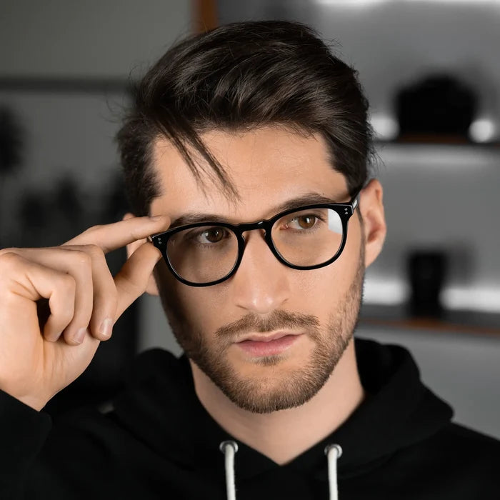 Man adjusting glasses with a blurred indoor background