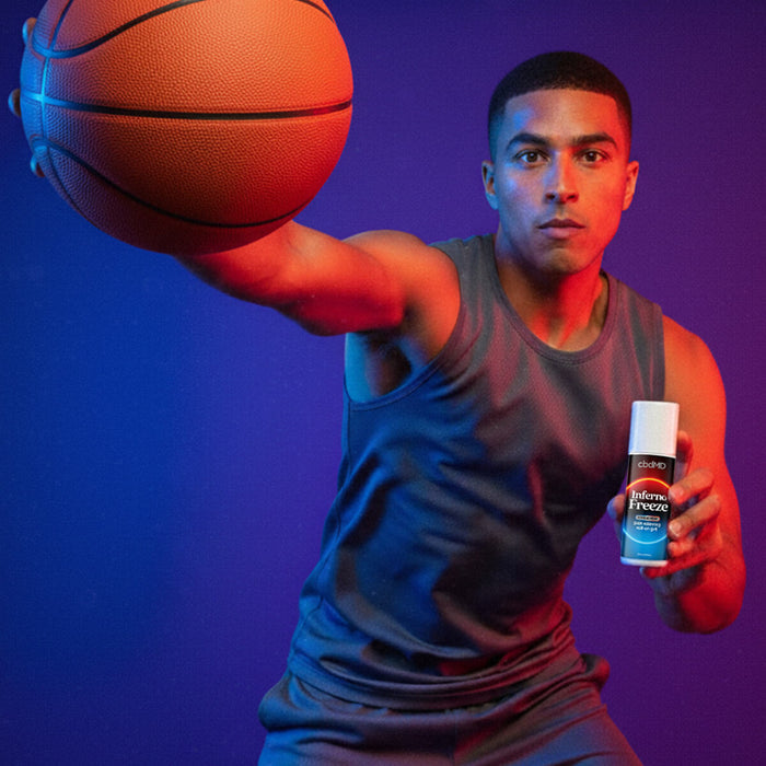 Athlete holding basketball and cbdMD Inferno Freeze pain relief roll-on