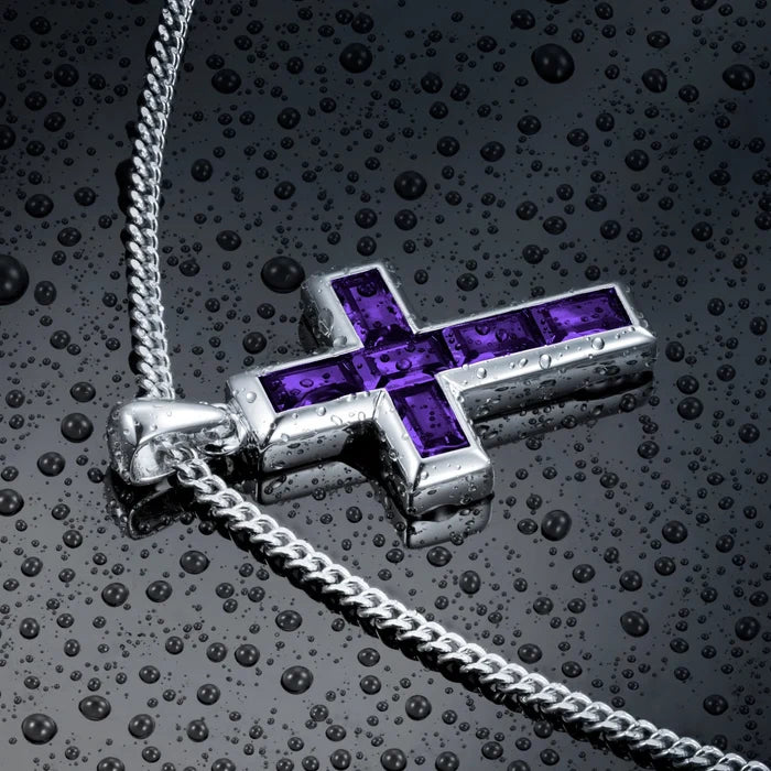 Silver cross pendant with purple stones on a textured black surface