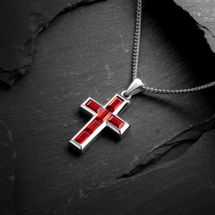 Silver cross pendant with red stones on a dark stone surface