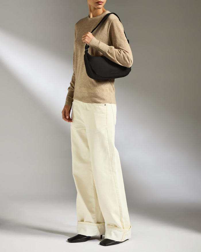 a woman in beige sweater and white pants holding a black purse