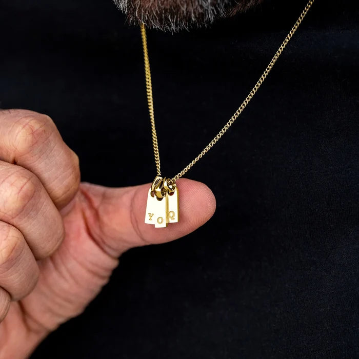 Gold necklace with a pendant held by a hand against a black background