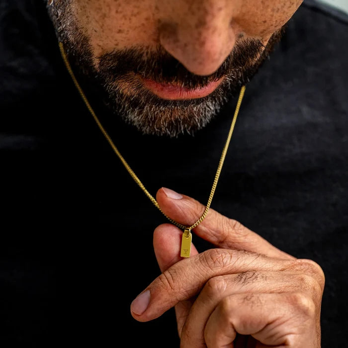 Man holding a gold necklace with a small tag against a black background