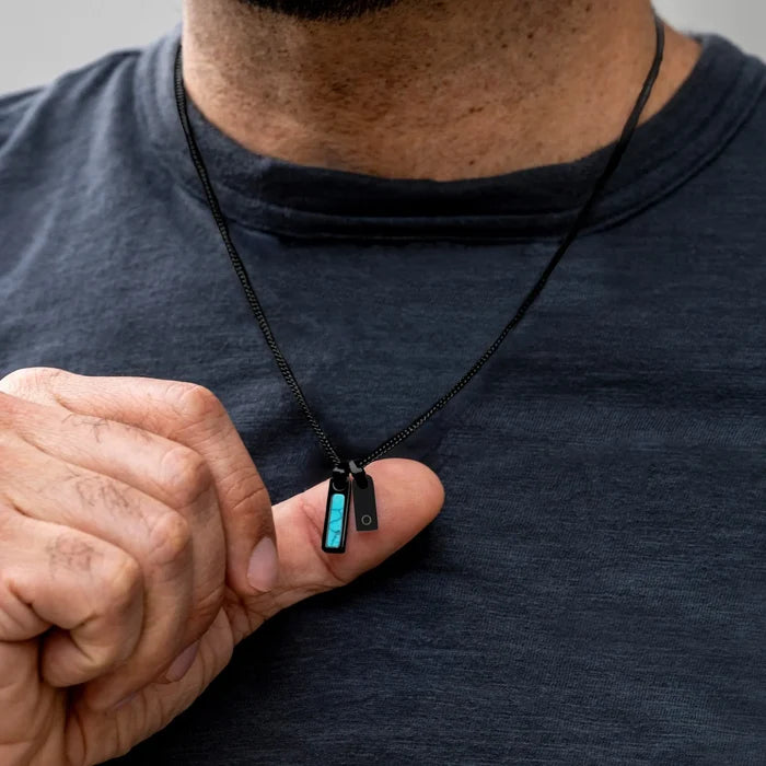 Person holding a small black electronic device with a blue light on a plain background