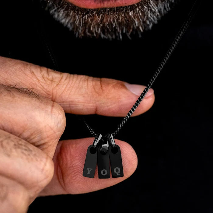 Black necklace with 'YOQ' pendant held by a hand against a dark background