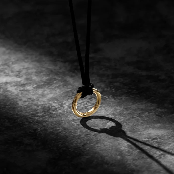 A 14K gold-colored pendant in the shape of a cross, attached to a black necklace cord, presented against a dark background.