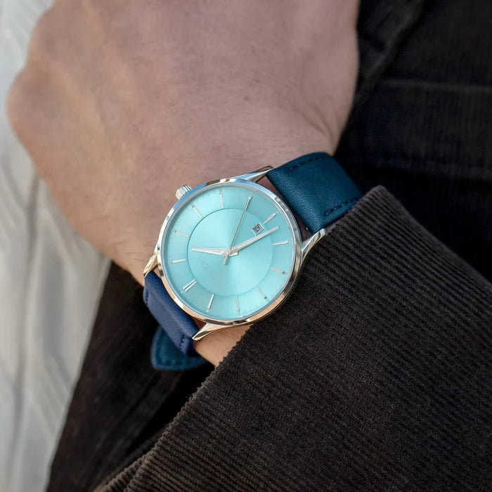 Watch with a blue strap and turquoise face on a wrist.