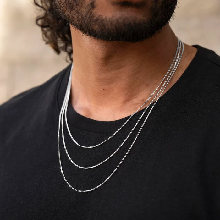 Man wearing two silver necklaces on a blurred background