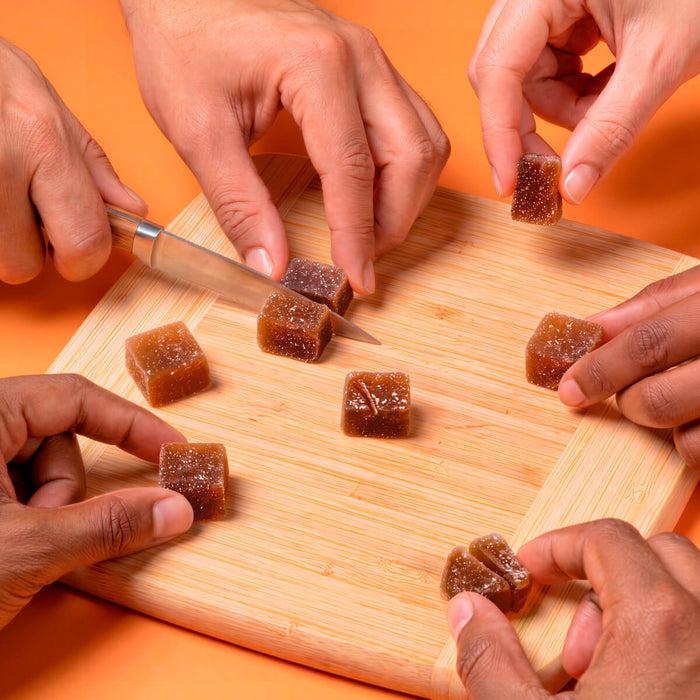 Hands cutting and sharing cbdMD tangerine THCv gummies on a wooden board.